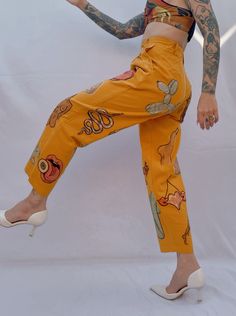 a woman in yellow pants with tattoos on her arms and legs, posing for the camera