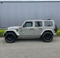 a grey jeep parked in front of a building with black tires and rims on it