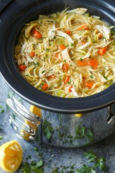 a pot filled with chicken noodle soup next to sliced lemons and parsley