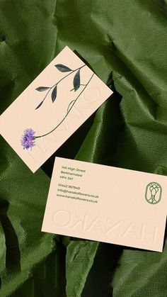 two business cards sitting on top of a green cloth covered in leaves and flowers, with the word hanko printed on them