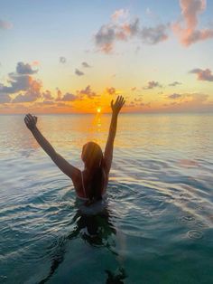 a woman standing in the water with her arms up and hands raised above her head