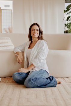 a woman sitting on the floor in front of a white couch smiling at the camera