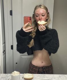 a woman taking a selfie in front of a bathroom mirror while holding food up to her face