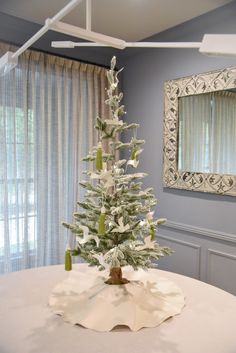 a white christmas tree on top of a table in a room with blue walls and curtains