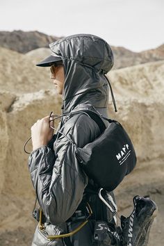 a man in grey jacket and black hat with backpack on his back walking through the desert