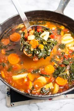 a ladle full of vegetable soup on top of a marble counter with a spoon