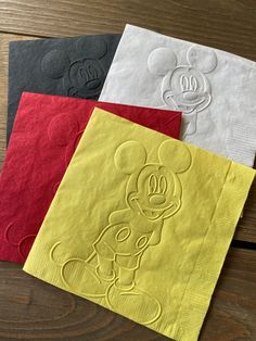 four napkins with mickey mouse designs on them are sitting on a table top, one is yellow and the other is red