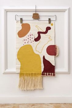 a painting hanging on a white wall next to a wooden hanger with fringes