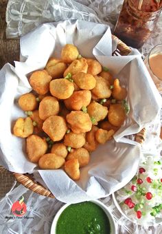 a basket filled with tater tots next to a bowl of green dipping sauce