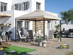 an outdoor dining area with chairs, tables and a grill in the back ground next to a house