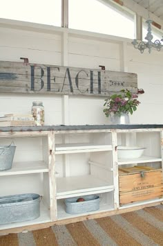 an old wooden shelf with baskets and buckets on it in front of a beach sign