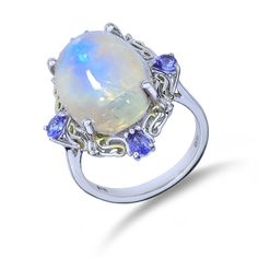 "**All photos are professionally photographed in our in-house studio, and are of the exact item you will receive.** **All measurements done in inches are rounded to the nearest 1/8\". ** The ethereal blue phenomenon of a moonstone is nicely paired with 4 tanzanite in the sterling silver halo setting on this ring. Metal Type: Sterling Silver Hallmarks: 925, STS Metal Finish: High Polish Ring Size: 8.25 Setting: Prong Item Weight: 6.50 grams Center Gemstone Gemstone: Moonstone Shape: Oval Cabochon Oval Opal And Moonstone Multi-stone Ring, Oval Opal Multi-stone Ring With Moonstone, Formal Sterling Silver Moonstone Birthstone Ring, Formal Fine Jewelry Moonstone Ring With Gemstone Accents, Silver Tanzanite Multi-stone Rings, Elegant Blue Hallmarked Moonstone Ring, Formal Opal Moonstone Ring, Silver Tanzanite Gemstones With Accents, Silver Multi-stone Moonstone Ring