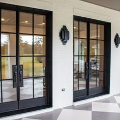 two black double doors on the side of a white building with checkered flooring