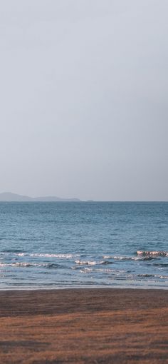 a person walking on the beach with a surfboard in their hand and an island in the distance