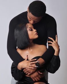 a man and woman embracing each other with their arms around one another, both wearing black