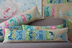 three pillows on a couch in front of a floral wallpaper