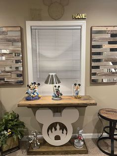 a mickey mouse lamp on top of a wooden table in front of a large window