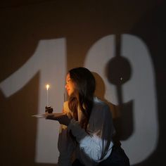 a woman holding a plate with a cake on it and lit candle in front of her