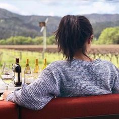 a woman sitting at a table with wine bottles and glasses in front of the window