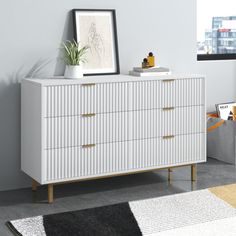 a white dresser with gold handles and drawers in a modern living room, next to a potted plant