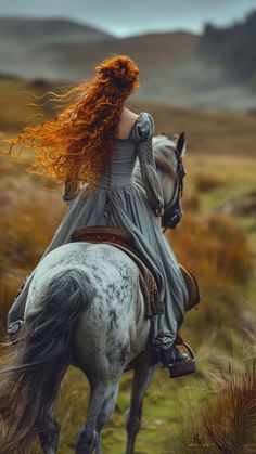 a woman with red hair riding on the back of a white horse in a field