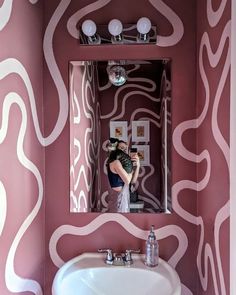 a woman taking a selfie in a bathroom mirror with pink and white wallpaper