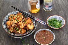 two bowls of food and chopsticks on a wooden table with condiments