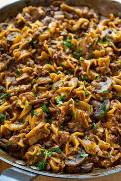 a skillet filled with pasta and meat covered in sauce, parsley on the side