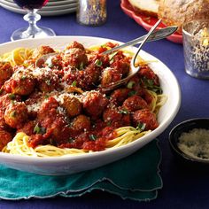 a bowl of spaghetti with meatballs and parmesan cheese on the side next to bread