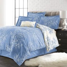 a bed with blue comforters and pillows in a room next to a window,