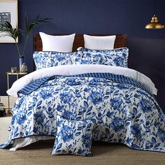 a bed with blue and white comforters in a room next to a plant on the wall