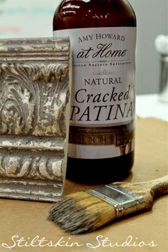 a bottle of wine next to a paintbrush on a wooden table with the words cracked patina