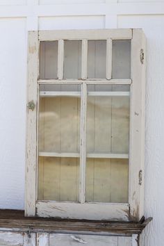 an old window sitting on top of a wooden shelf in front of a white wall