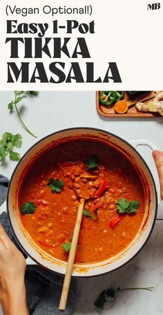 a person holding a wooden spoon in a pot filled with red curry and garnished with cilantro