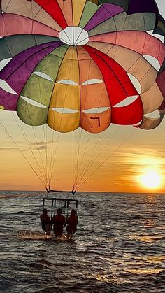 a group of people riding on top of a parachute over the ocean at sunset or dawn