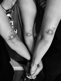 two people are holding hands with tattoos on their arms and one has the sun above them