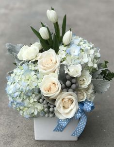 a bouquet of white and blue flowers in a square vase on the ground with a ribbon