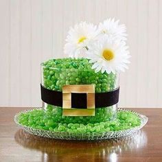 a green cake with white flowers on top sitting on a table next to a glass plate