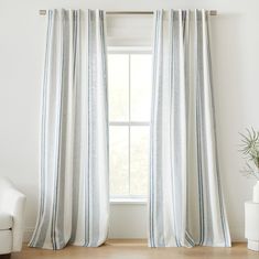 a white chair sitting next to a window in a room with striped drapes on the windowsill