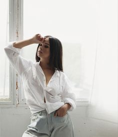 a woman in white shirt and jeans leaning against a window