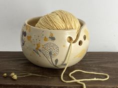 a ball of yarn in a bowl on a wooden table next to a knitting needle