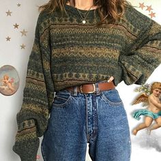 a woman standing in front of a wall wearing jeans and a sweater with an angel painting on it