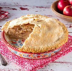 a pie sitting on top of a red and white plate next to a bowl of apples