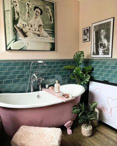 a pink bath tub sitting next to a green plant in a bathroom with pictures on the wall