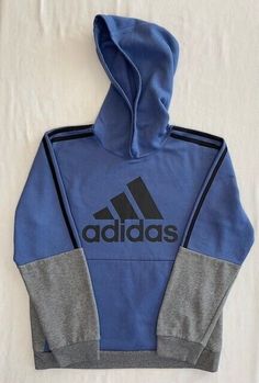 This Adidas Youth Pullover Fleece Hoodie in Blue/Heather Grey is perfect for any active boy. The hoodie is made of a soft and comfortable blend of 58% cotton and 42% polyester fleece, making it easy to care for. The hoodie features a logo on the front, a pullover style. It also has pockets for convenience. The hoodie is a size Large (14/16) and has a chest size of approximately 36 inches in circumference. The sleeves length from shoulder to hem is around 23.5 inches, while the length from top to bottom, excluding the hood, is approximately 21.5 inches. The sleeves from shoulder to hem measures around 23 inches. The hoodie is ideal for walking, school, activewear, running and jogging, and casual wear. Sporty Navy Hoodie For Fall, Blue Color Block Sweatshirt Athleisure Style, Sporty Blue Hoodie For Winter, Adidas Hooded Sweatshirt For Fall, Blue Color Block Sweatshirt For Winter, Fall Sports Hoodie With Color Block, Sporty Blue Hoodie For Fall, Blue Athleisure Hoodie For Winter, Blue Athleisure Hoodie For Fall