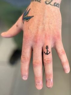 a hand with a small anchor tattoo on it's left thumb and the word love is written in black ink