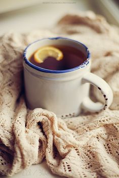 a cup of tea with a lemon slice in it sitting on a blanket next to a window