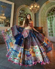 a woman standing in front of a chandelier wearing a colorful dress with an intricate pattern