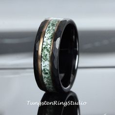 a wedding band with green moss inlays and black ceramic, on a reflective surface