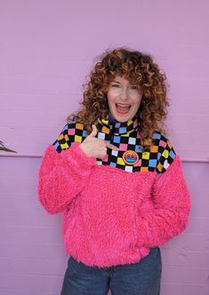 a woman with curly hair wearing a pink fuzzy sweater and giving the thumbs up sign